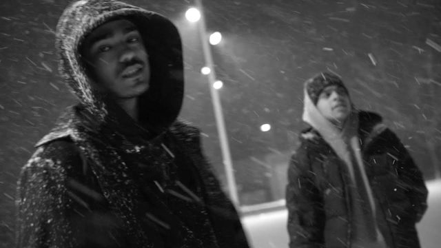 Still from the Time video: two figures in hooded coats in falling snow
